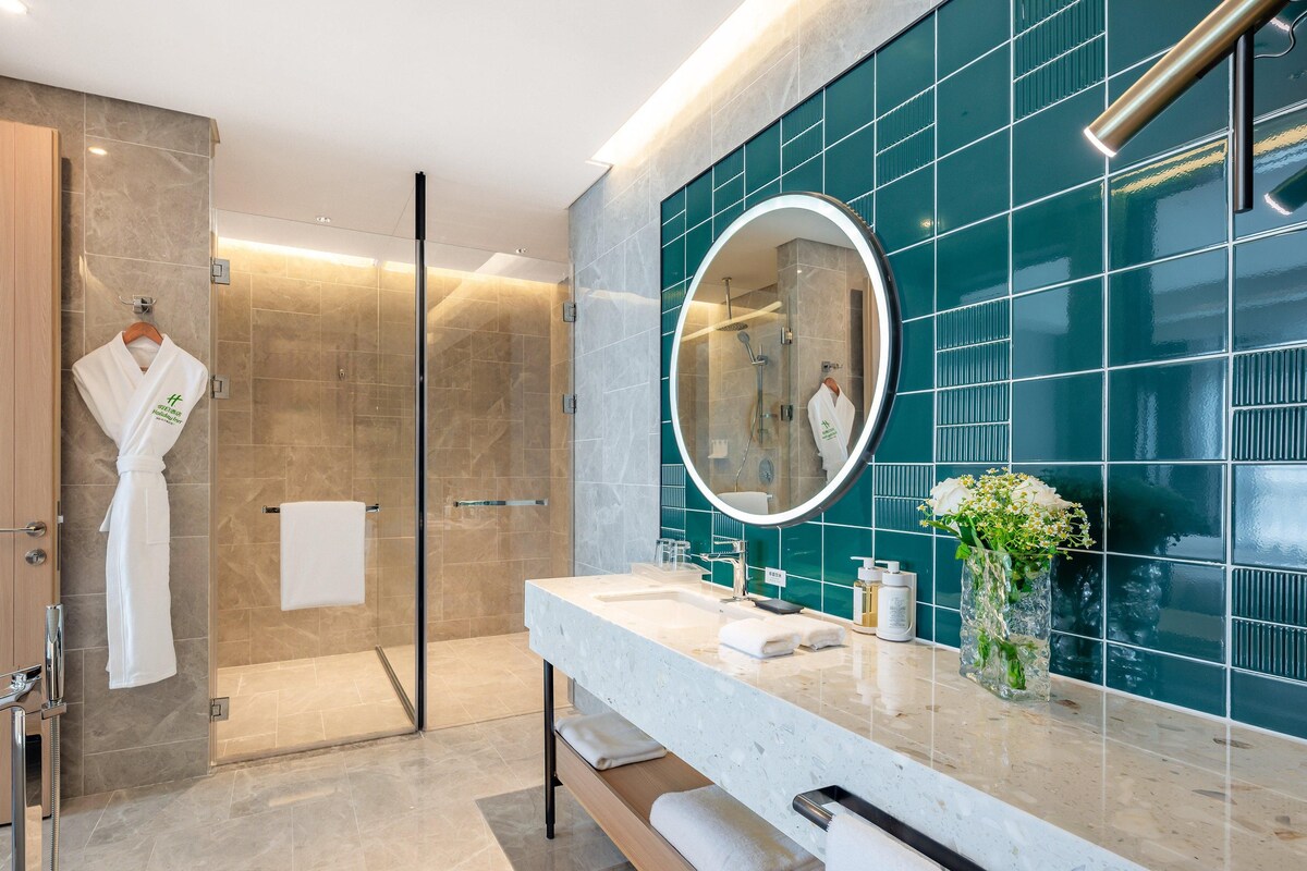 A modern bathroom with a glass shower, a round mirror, and a marble sink.