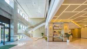 En rummelig lobby med en central trappe, en receptionsdisk og et moderne loftdesign.