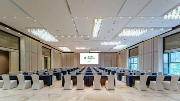 A conference room with rows of tables and chairs, a large screen at the front, and a modern chandelier.