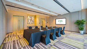 Ein Konferenzraum mit langem Tisch, Stühlen, einer Projektionsleinwand und einem Blumentopf.