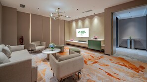 Eine moderne Hotelhalle mit Empfangsschalter, Sitzgelegenheiten und einem großen Bildschirm, der Informationen zeigt.