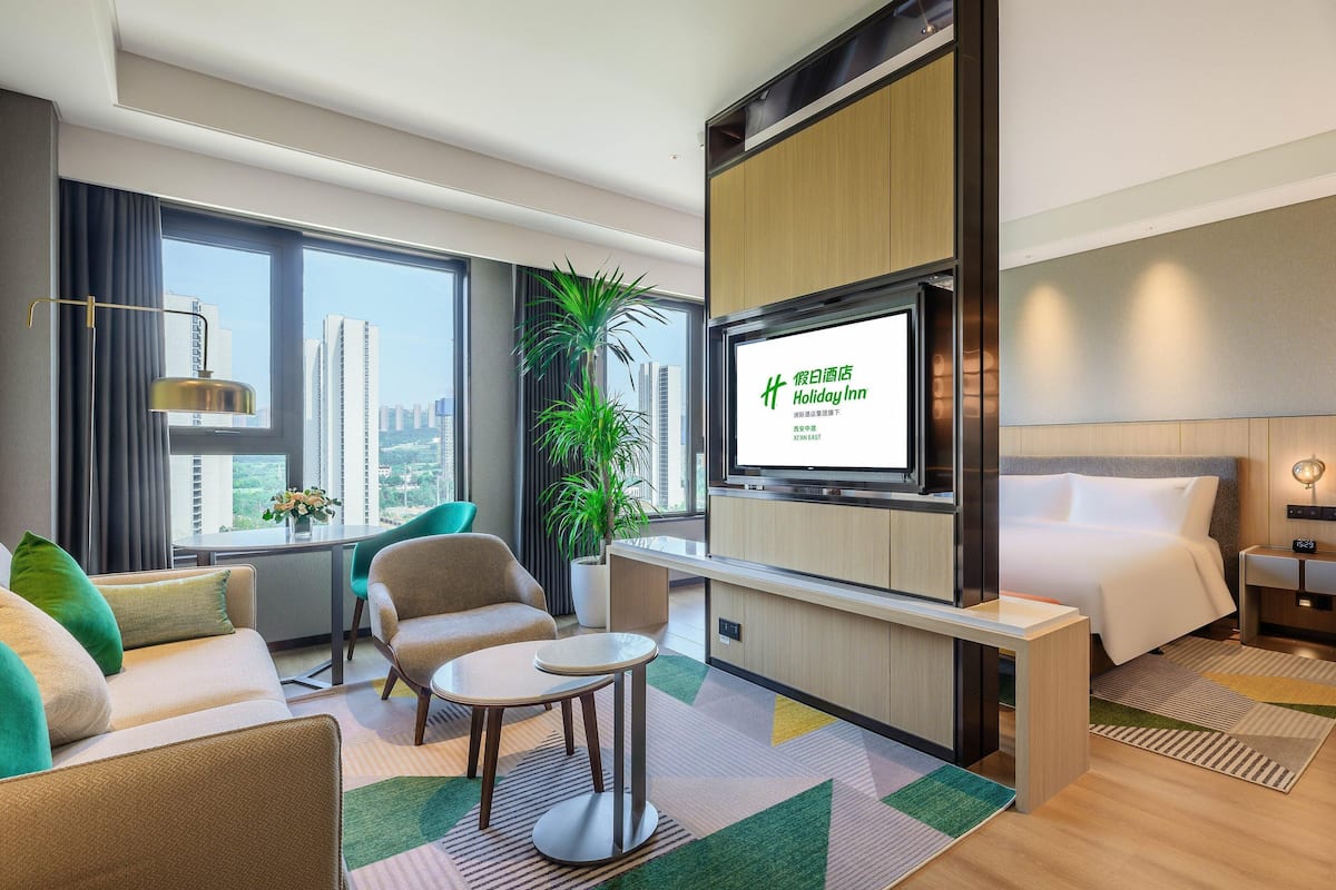 Une chambre d’hôtel moderne équipée d’un lit, d’un bureau, d’une chaise, d’une télévision et d’une grande fenêtre donnant sur la ville.