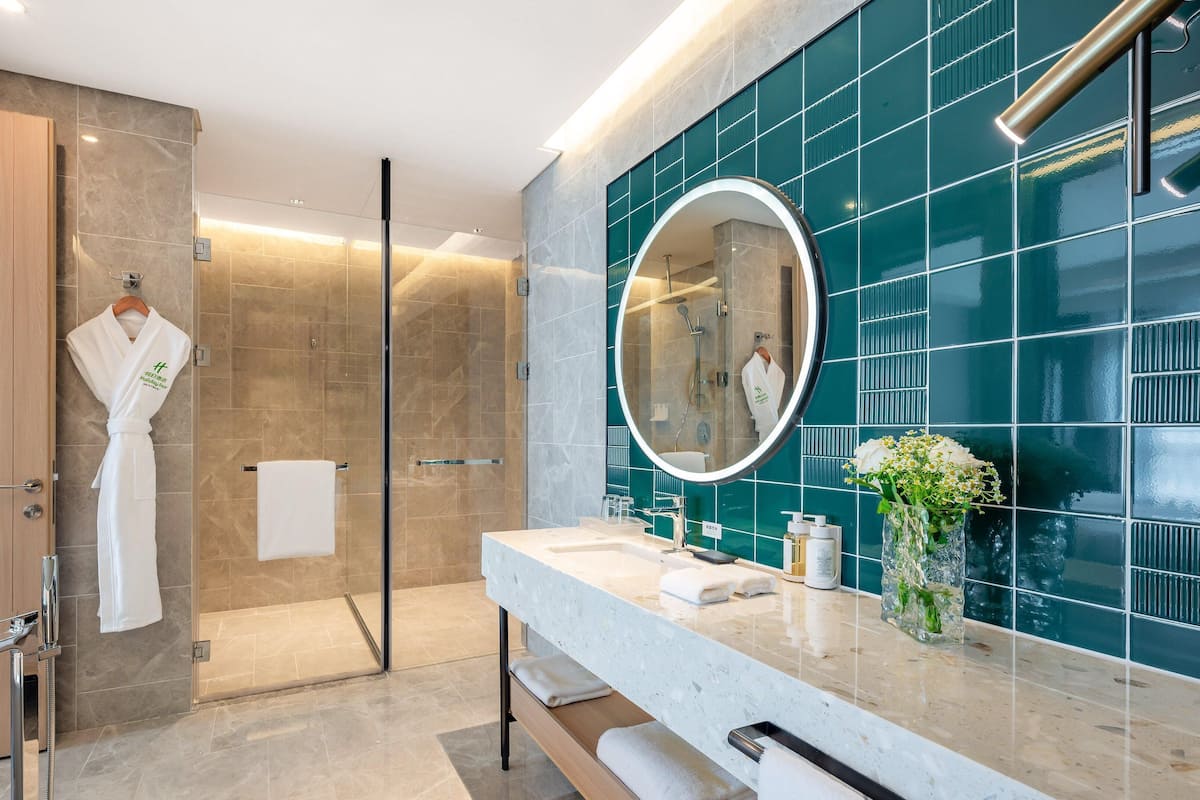 Une salle de bain moderne avec une douche en verre, un miroir rond et un lavabo en marbre.