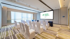 A conference room with rows of white chairs, a projection screen, and a large window with curtains. - Holiday Inn Xian East (Xi'an)