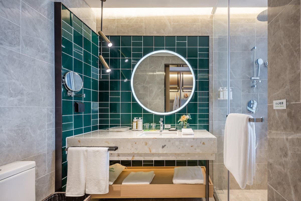 Une salle de bain moderne avec un grand miroir rond, un lavabo et une douche.