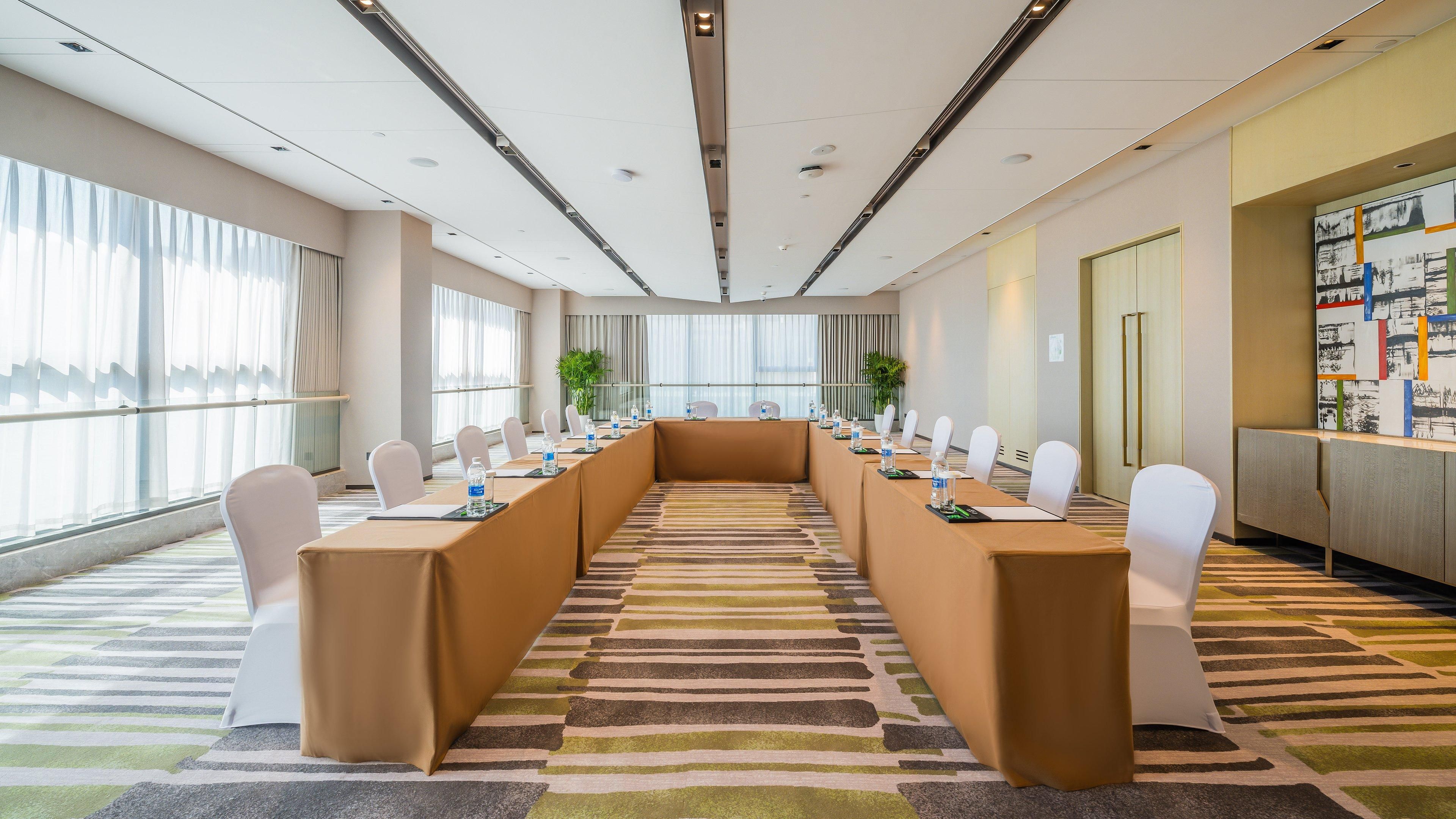 Una sala conferenze con un lungo tavolo, sedie bianche e una moquette a motivi.