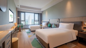 A modern hotel room with a large bed, a desk, a chair, and a view of tall buildings through the window. - Holiday Inn Xian East (Xi'an)