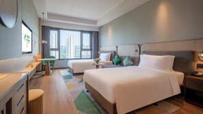 A modern hotel room with a large bed, a desk, a chair, and a view of tall buildings through the window. - Holiday Inn Xian East (Xi'an)