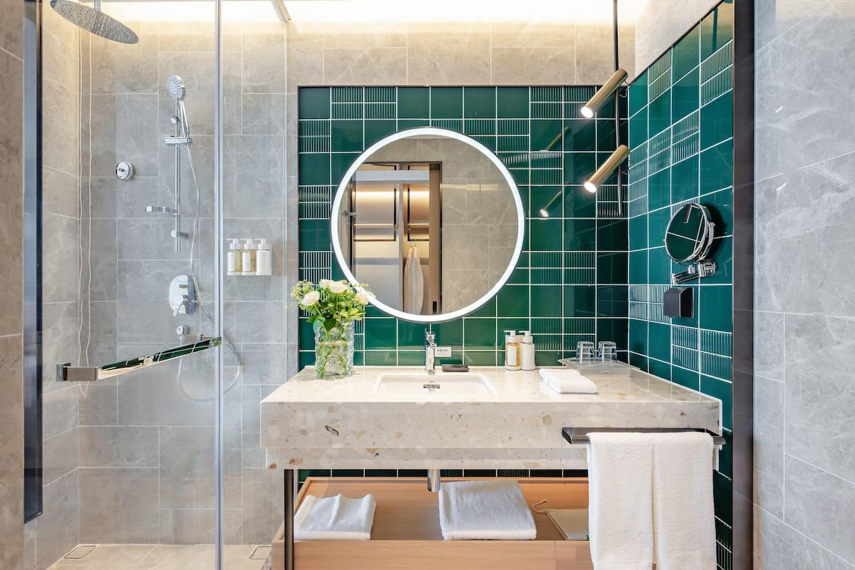 Une salle de bain moderne dotée d’une douche à parois de verre, d’un miroir rond et d’un meuble-lavabo avec un évier et un porte-serviettes.
