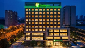 Et Holiday Inn hotel med flere etager, et tydeligt grønt skilt og en velbelyst facade.