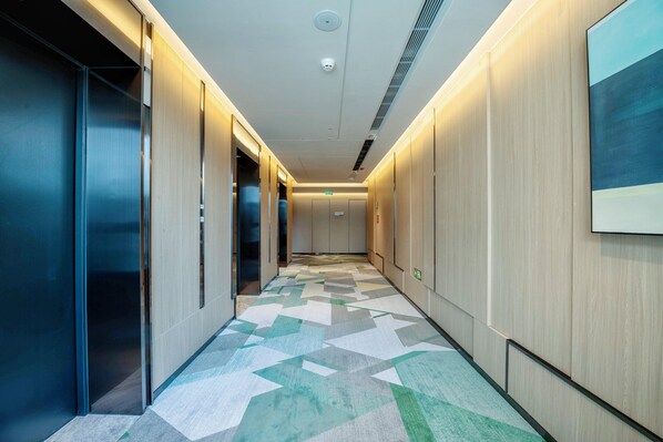 A modern hallway with a geometric patterned floor, wooden panel walls, and a ceiling with recessed lighting and a smoke detector. - Holiday Inn Xian East (Xi'an)