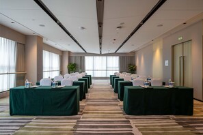 A conference room with rows of tables, chairs, and water bottles, featuring a carpeted floor and large windows. - Holiday Inn Xian East (Xi'an)