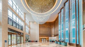 A spacious lobby with a high ceiling, large windows, and a central chandelier.