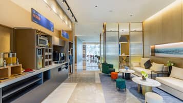 A modern hotel lobby with a kitchen area, seating, and a large window.