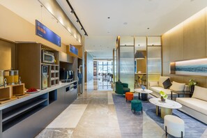 A modern hotel lobby with a kitchen area, seating, and a large window. - Holiday Inn Express Zhoukou Dancheng An Ihg Hotel (Zhoukou)