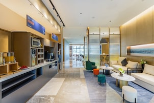 A modern hotel lobby with a kitchen area, seating, and a large window.