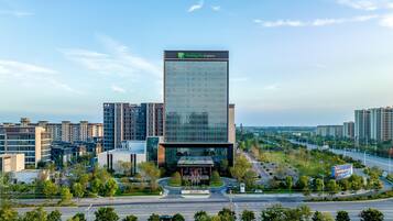 A modern Holiday Inn Express hotel with a glass facade, surrounded by urban buildings and greenery.