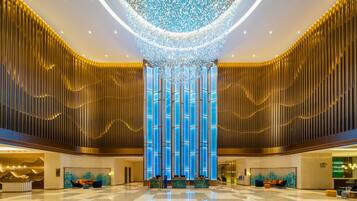 A spacious lobby with a high ceiling, a central blue-lit column, and a reception desk.