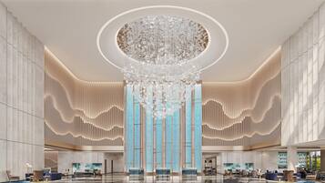 A spacious lobby with a large chandelier, vertical wooden slats, and a blue patterned wall.