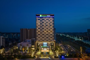 Un hotel Holiday Inn Express con un diseño moderno, que presenta un letrero llamativo en la parte superior y una entrada bien iluminada.