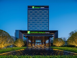 A Holiday Inn Express hotel with a modern glass facade, a covered entrance area, and well-lit outdoor seating. - Holiday Inn Express Zhoukou Dancheng An Ihg Hotel (Zhoukou)