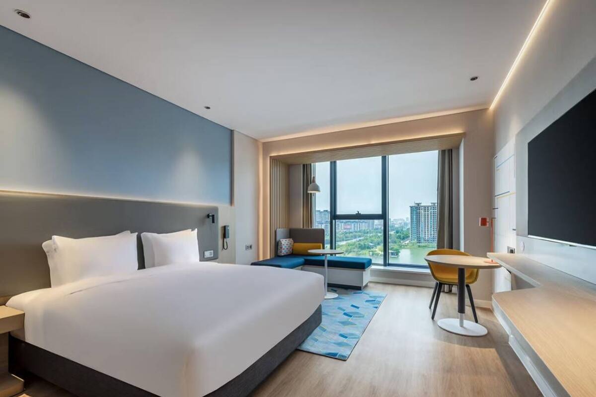 A modern hotel room with a large bed, a seating area with a view, and a small table.