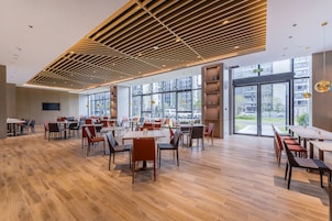 Un comedor amplio con suelo de madera y mobiliario moderno, ventanas grandes que ofrecen vistas a la ciudad y un techo con diseño geométrico.