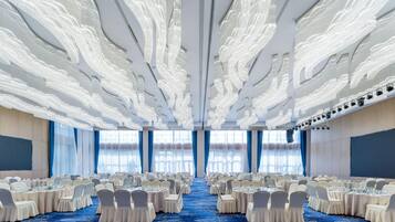 A banquet hall with round tables, white chairs, and a blue carpet.