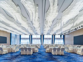 A banquet hall with round tables, white chairs, and a blue carpet.