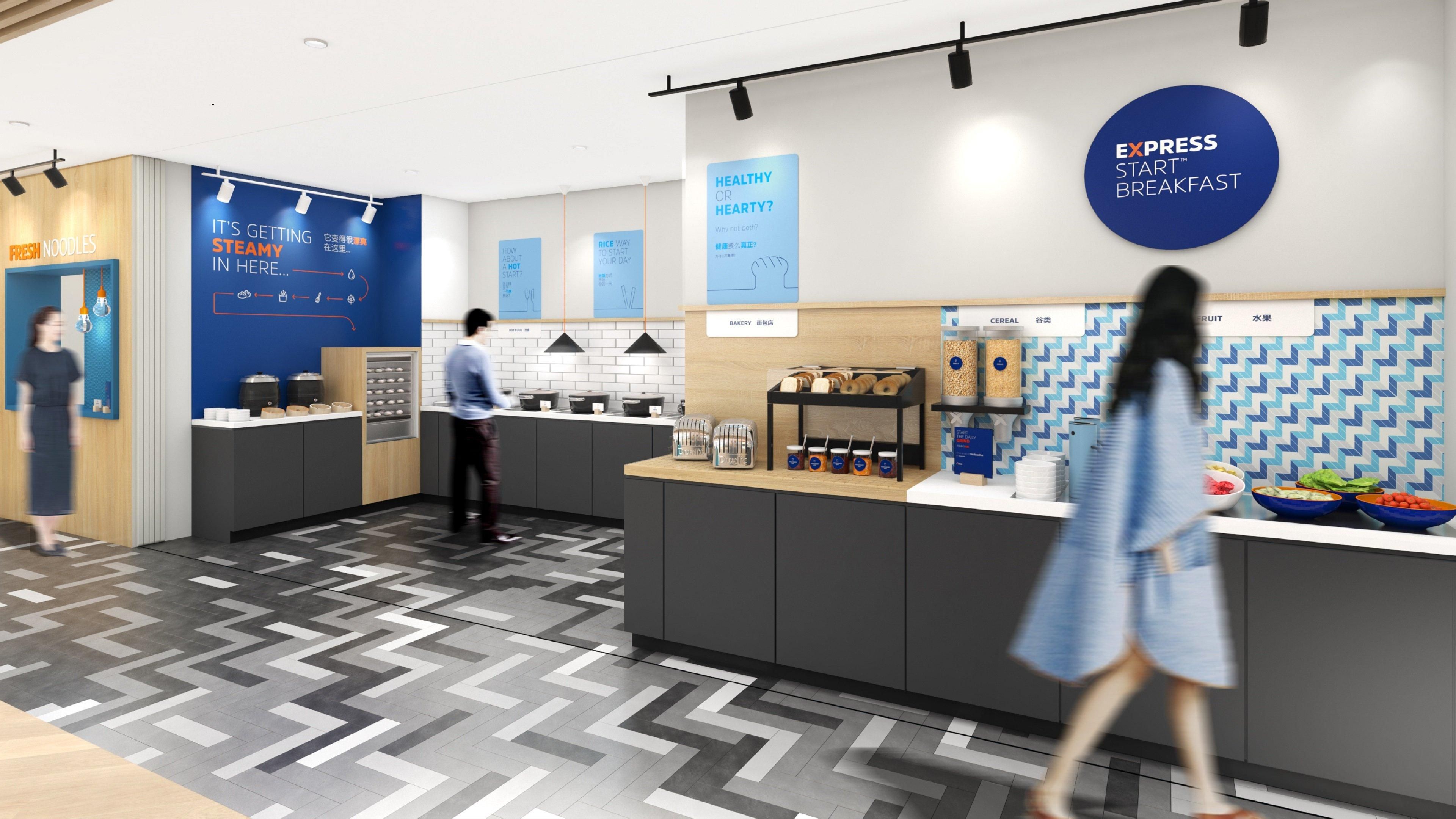 A modern breakfast area with a counter displaying fresh juices, cereals, and fruits. There are signs about healthy eating and a digital display for ordering.