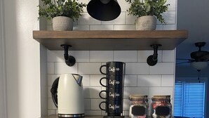 Una cocina con cafetera, tazas y plantas en macetas sobre estantes.