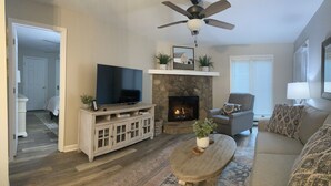 Una sala de estar con chimenea de piedra, un televisor sobre un mueble, un ventilador de techo y un sofá.
