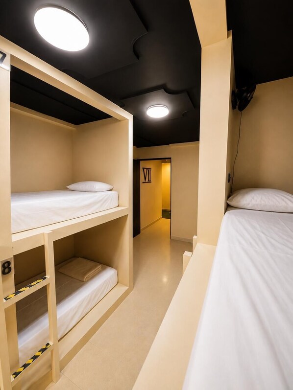 Habitación de hotel con literas, una puerta visible con un número y una lámpara en el techo.