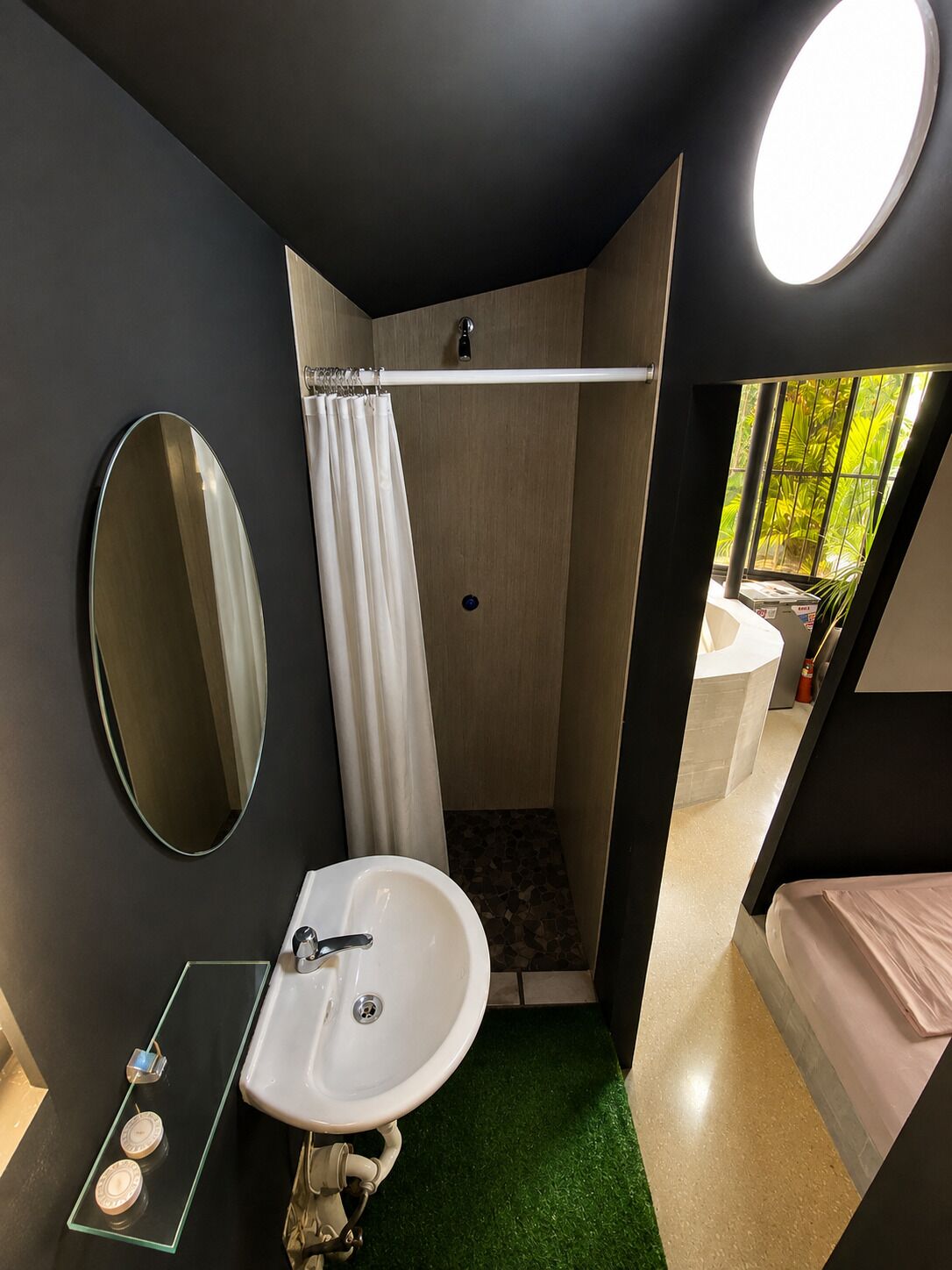 Une petite salle de bain comprenant un lavabo, un miroir, une douche et une petite fenêtre.