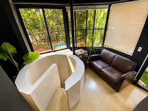 Un interior moderno con una estructura blanca curva, un sofá de cuero marrón y grandes ventanas con vistas al verdor.