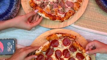 Duas pizzas sobre tábuas de madeira, um smartphone e um copo de água em uma mesa.