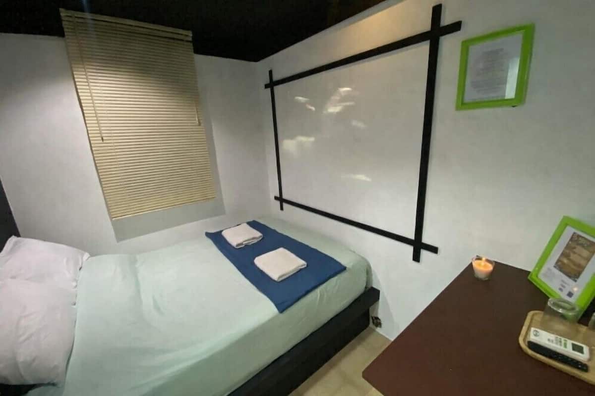 Une pièce comprenant un lit, un écran de projection fixé au mur, une petite table avec une télécommande et une bougie.