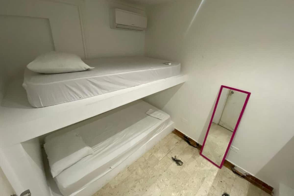 Une chambre avec un lit superposé, un miroir et une porte.