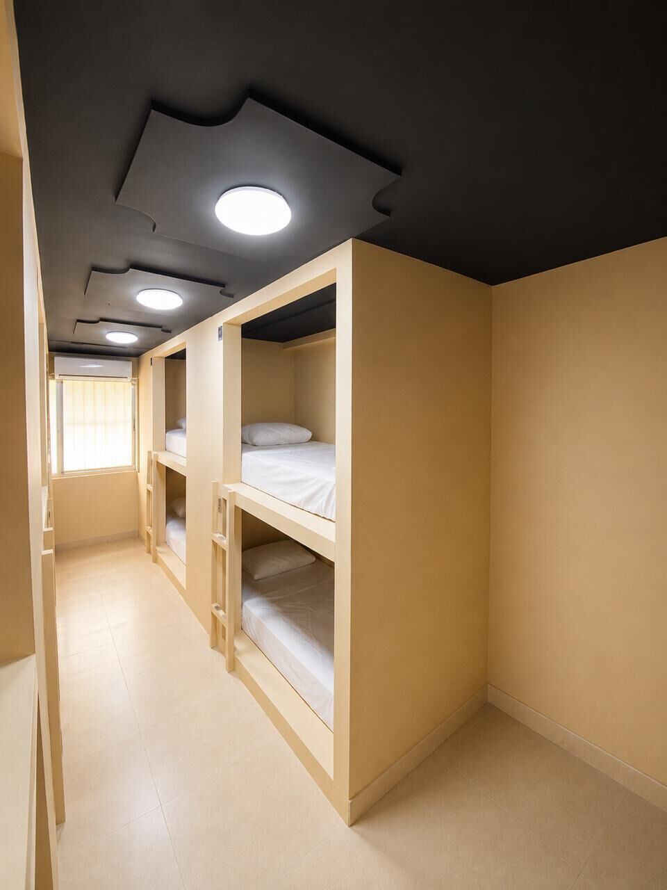 Une chambre avec des lits superposés, un plafond doté d’un éclairage encastré et une fenêtre avec des stores.