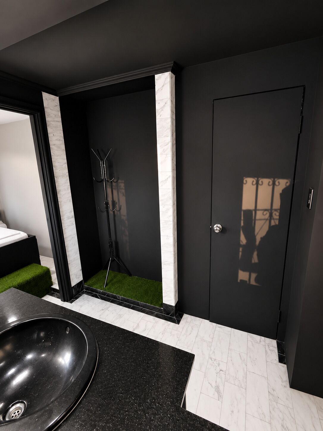 Moderni kylpyhuone, jossa on musta pesuallas, valkoiset marmorilaatat ja ovi, joka luo varjoja.
