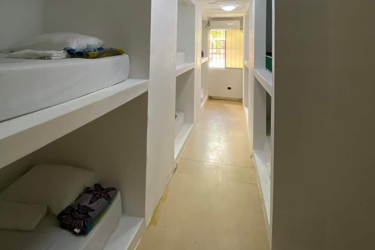 Un couloir étroit, avec des lits superposés de chaque côté, un sol carrelé et des spots encastrés au plafond.