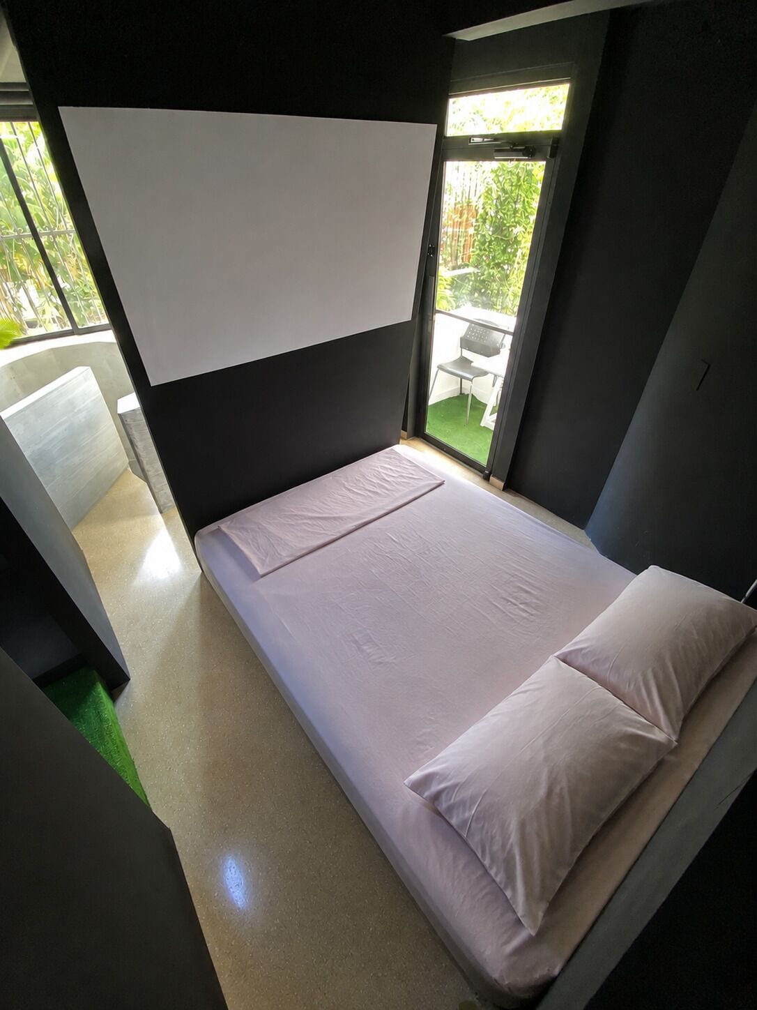 Una habitación pequeña con cama individual, ventana, una silla y un tapete verde.