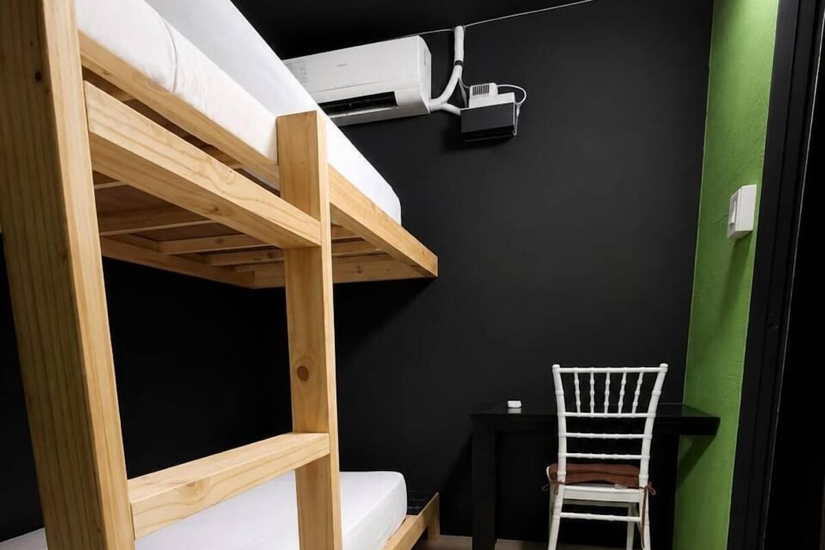 Un lit superposé avec un matelas blanc, un bureau avec une chaise et un appareil de climatisation fixé au mur.