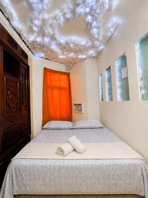 A hotel room with a bed, a wooden dresser, a window with curtains, and a ceiling with decorative lights. - Panamá Experience Hostel (Panama City)