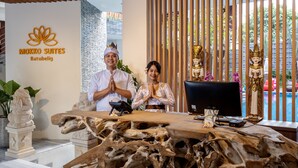A reception desk with a wooden top, a computer, and a statue of a deity. The reception area has a sign for MOKKO SUITES Batubelig. - Mokko Suites Batubelig (Keroboken Kelod)