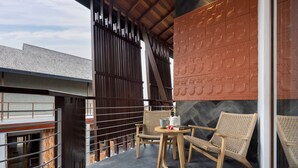 A balcony with two wicker chairs, a small round table, and a decorative wall with embossed patterns. - Mokko Suites Batubelig (Keroboken Kelod)