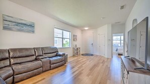 A spacious living room with a brown leather sofa, hardwood flooring, and a large window. -  Home with Private Heated Pool 10 Mi to Disney World and other Major Parks! (Davenport)