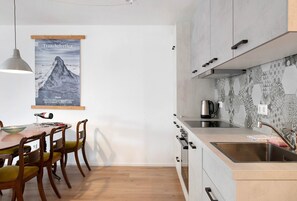 A modern kitchen with a wooden dining table, chairs, a hanging light, and a poster on the wall.