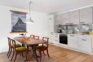 A modern kitchen with white cabinets, a wooden dining table, and a poster of a mountain.