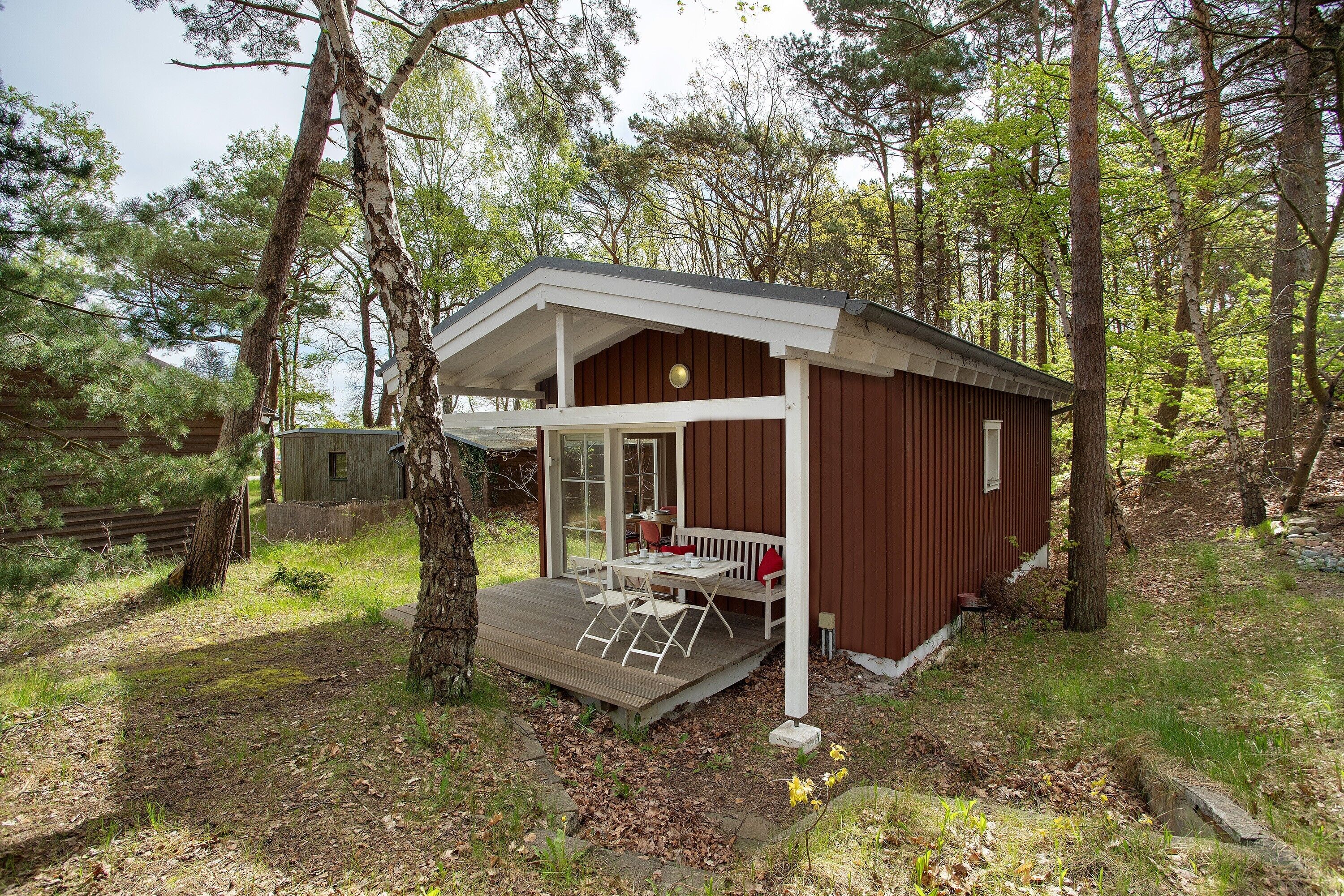 Eine Holzhütte mit einer Holzterrasse, einer überdachten Veranda und einem Fenster mit Blick auf den Wald.